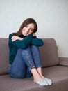Pretty brunette woman with magnificent eyes and adorable smile in green sweater and blue jeans relaxing sitting on sofa hugging Royalty Free Stock Photo