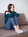 Pretty brunette woman with magnificent eyes and adorable smile in green sweater and blue jeans relaxing sitting on sofa hugging Royalty Free Stock Photo