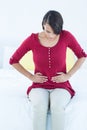 Pretty brunette sitting on bed with stomach pain Royalty Free Stock Photo