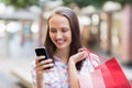 Pretty brunette using her smartphone and holding shopping bag Royalty Free Stock Photo