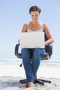 Pretty brunette using laptop on the beach sitting on swivel chair