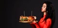 Pretty brunette woman with closed eyes and pouty lips in red bodysuit holds two fresh big burger on wooden tray. Banner