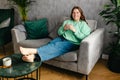 Pretty brunette woman drinking water on couch at home in the living room. 30s female rest and spend free spare time Royalty Free Stock Photo