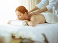Pretty brunette woman enjoying procedure of back massage in sunny spa salon. Beauty concept. Cold toned picture