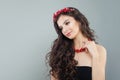 Pretty brunette woman with makeup, long curly hair and red coral necklace on gray background