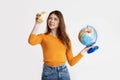 A pretty brunette in a yellow sweater holds a globe in her hands and looks into the camera`s viewfinder. Recreation, travel,