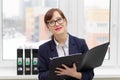 pretty business woman in glasses in a light office near the window with a folder in her hands makes notes. portrait Royalty Free Stock Photo