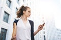 Pretty business woman hold paper documents and search financial news on screen smartphone stand among urban space Royalty Free Stock Photo