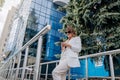 Pretty business woman in white suit and sunglasses using phone during break standing near modern office building Royalty Free Stock Photo