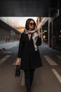 Pretty business young woman model with elegant scarf on head in fashionable sunglasses in a trendy coat with leather black handbag Royalty Free Stock Photo