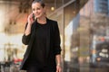 Pretty businesswoman talking on cellphone or mobile phone while walking on busy city street Royalty Free Stock Photo