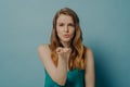 Pretty candid girl blowing air kiss and expressing love while standing isolated on blue background Royalty Free Stock Photo