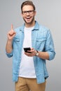 Pretty casual man in blue jeans shirt holding his phone standing over studio grey background Royalty Free Stock Photo