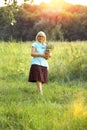 A pretty Caucasian 60+ elderly and beautiful woman with white hair walking in nature with a bouquet of wild flowers. Enjoyment and