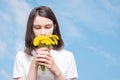 Pretty caucasian girl inhales the scent of yellow dandelions against a blue sky with clouds, copy space. The girl Royalty Free Stock Photo