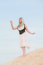 Young beautiful Caucasian woman in white dress and brown leather waistcoat posing in desert landscape with sand. Royalty Free Stock Photo