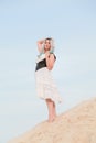 Young beautiful Caucasian woman in white dress and brown leather waistcoat posing in desert landscape with sand. Royalty Free Stock Photo