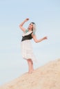 Young beautiful Caucasian woman in white dress and brown leather waistcoat posing in desert landscape with sand. Royalty Free Stock Photo