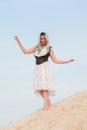 Young beautiful Caucasian woman in white dress and brown leather waistcoat posing in desert landscape with sand. Royalty Free Stock Photo