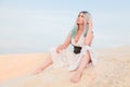 Young beautiful Caucasian woman in white dress and brown leather waistcoat posing in desert landscape with sand. Royalty Free Stock Photo