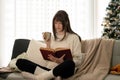 A pretty caucasian woman is reading a book and sipping coffee on a couch in her living room