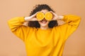 Pretty charming joyful attractive cheerful funny comic positive curly girl having two pieces of orange, isolated on beige Royalty Free Stock Photo