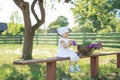 Pretty cheerful child is sitting on a bench in garden with a basket filled with purple lilac flowers. Royalty Free Stock Photo