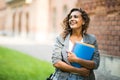 Pretty cheerful student smiling at camera carrying notebook on campus at college Royalty Free Stock Photo