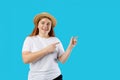 Pretty cheerful woman in straw hat gesturing with fingers and showing away isolated over blue background, studio Royalty Free Stock Photo