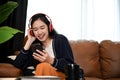 Pretty Asian female listening to music through her headphones while relaxing in the living room Royalty Free Stock Photo