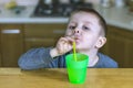 Pretty child drinks a soft drink through a plastic straw in the kitchen. Portrait of beautiful little boy in kitchen at home. Royalty Free Stock Photo