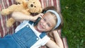 Pretty child girl laying on green lawn with her teddy bear talking on mobile phone Royalty Free Stock Photo