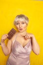 Pretty chubby girl with chocolate bar on yellow studio solid background