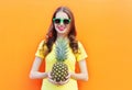 Pretty cool smiling girl in sunglasses with pineapple over colorful orange Royalty Free Stock Photo