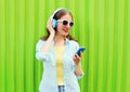 Pretty cool woman listens to music in headphones using smartphone over green