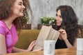 Pretty curly woman making present to female friend in cafe Royalty Free Stock Photo