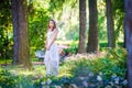 Pretty curvy brunette girl with long hair in white long dress standing in the green forest. Fairy princess stands on woods Royalty Free Stock Photo