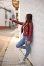 Pretty curvy girl taking a selfie with the smartphone in the street next to a peculiar white wall