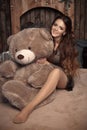 Pretty cute brunette girl posing with big teddy bear on the floor in cozy comfortable interior home.