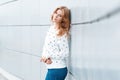 Pretty cute happy young woman with a fashionable hairstyle in a stylish sweater in blue trendy jeans relaxes standing