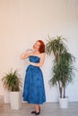 Mannered beautiful vintage woman dressed in blue retro dress standing alone in the empty white room