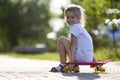 Pretty cute little blond girl in white shorts and T-shirt sitting on pink skateboard and smiling in camera on a light blurred Royalty Free Stock Photo