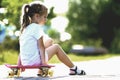 Pretty cute little blond girl in white shorts and T-shirt sitting on pink skateboard and smiling in camera on a light blurred Royalty Free Stock Photo