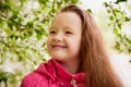 Pretty cute little girl with long hair posing near a blooming apple tree with white flowers in a summer park Royalty Free Stock Photo