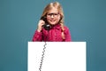 Pretty, cute little girl in pink shirt, black trousers and glasses holds empty poster and having a phone talk Royalty Free Stock Photo