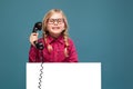 Pretty, cute little girl in pink shirt, black trousers and glasses holds empty poster and having a phone talk Royalty Free Stock Photo