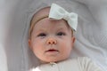 A beautiful cute serious baby girl in a beige bodysuit with a white bow on her head lies in a cradle on a white sheet. Royalty Free Stock Photo