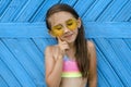 Pretty cute smiling brunette girl in yellow sunglasses and a swimsuit stands with a thoughtful look, putting her index finger to h Royalty Free Stock Photo