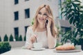 Pretty, cute, smiling woman in classic outfit sitting having breakfast, brunch in cafe terrace, talking with lover on smart Royalty Free Stock Photo