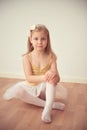 Pretty diligent ballet girl sitting in white tutu at dance studio